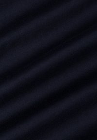 Tamsiai mėlyna medžiaga su lygiu paviršiumi, turinti subtilius griovelių raštus ir nedidelį blizgesį, krintanti per paviršių.