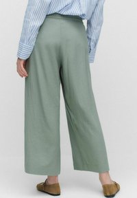 Brei-brede groene broek van lichtgewicht stof, met een hoge taille en een gladde textuur, gecombineerd met bruine schoenen en een blauw gestreept shirt.