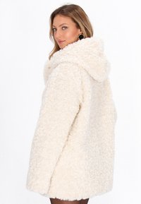 Cappotto di pelliccia finta color crema con una superficie texturizzata e soffice, dotato di un ampio cappuccio e di una vestibilità morbida, che arriva all'altezza della coscia.