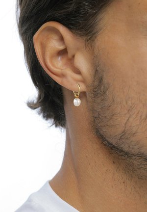 Gros plan sur l'oreille d'un homme portant une petite boucle d'oreille en or avec un pendentif unique en perle blanche.