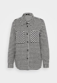 Camicia button-up in bianco e nero con motivo houndstooth, dotata di maniche lunghe, due tasche sul petto e un classico colletto.