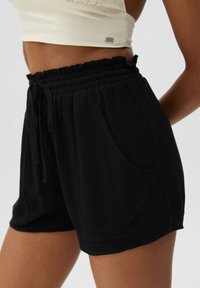 Pantalones cortos negros fabricados con un tejido ligero y texturizado. Incluyen una cintura elástica con cordón, bolsillos laterales y un ajuste holgado.