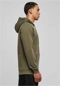 Felpa con cappuccio verde oliva, realizzata in tessuto morbido. Presenta una tasca frontale, polsini a coste e una vestibilità comoda.