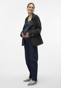 Svart trenchcoat med guldknappar, blå topp, mörka jeans och ljusblå spetsiga klackar. Ämnet har en synlig gravidmage.