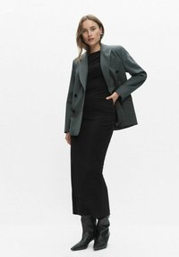 Szara marynarka dwurzędowa na czarnej sukience z marszczeniami, w połączeniu z czarnymi, wysokimi botkami na obcasie. Gładki materiał i dopasowany krój.