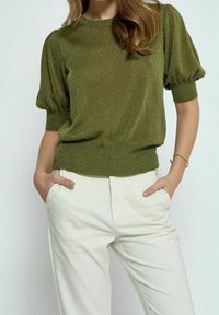 Olivgrön metallic stickad topp med kort puffärm och ribbade muddar, kombinerad med cremefärgade byxor. Avsmalnande passform med texturerad finish.