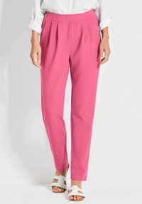 Roze geplooide broek van lichtgewicht stof met een zachte textuur. De pasvorm is tapered en is gecombineerd met witte sandalen met bandjes.