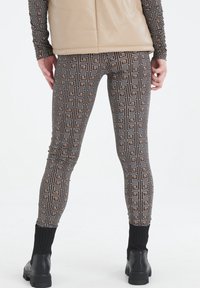 Mustat korkeavyötäröiset legginsit, joissa on geometrisia kuvioita kultaisena ja valkoisena. Venytettävä kangas, istuva malli, jossa on ribbireunat nilkoissa ja saappaissa.