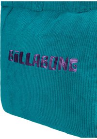 Turkusowa tkanina w prążki z haftowanym na fioletowo i lawendowo napisem "BILLABONG" w różnych odcieniach i stylach liter.