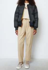 Puffy black jacket with yellow lining and pockets, beige high-waisted trousers, and chunky beige sneakers with brown accents.