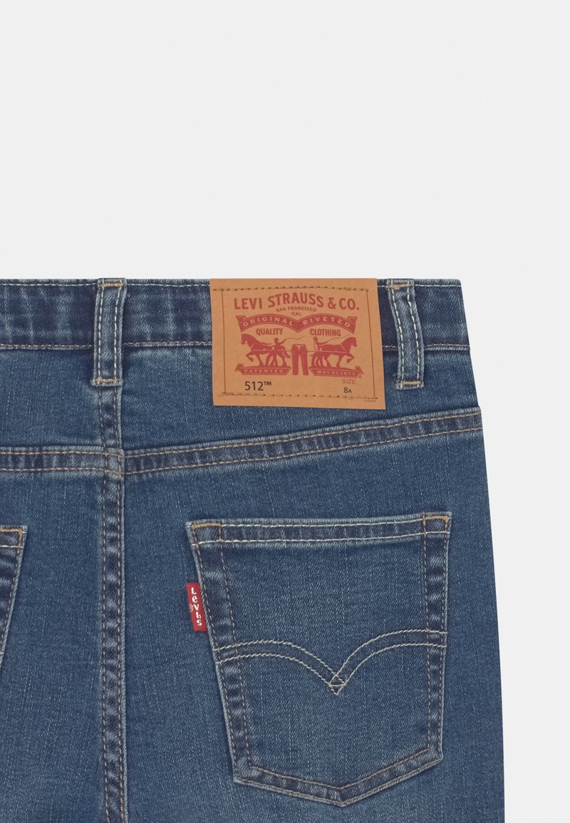 Jean Levi's 512 en denim bleu foncé. Comprend une patte en cuir marron avec un logo rouge à la taille, et une petite étiquette rouge sur la poche arrière.