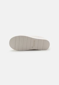 Suola di scarpa in gomma bianca con scanalature orizzontali e logo "GUESS" impresso. Texture liscia con una forma della punta leggermente arrotondata.