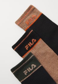 Tres pares de calcetines en negro, marrón y verde. Cada uno cuenta con una franja superior en contraste y el logo "FILA", resaltando la textura del material y el color.