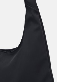 Černá látková taška přes rameno s hladkým povrchem, zaobleného tvaru a s jedním širokým popruhem. Švy na tašce dodávají vizuální zajímavost.