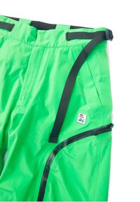 Pantalones impermeables verdes hechos de nylon texturizado, que presentan una cinturilla ajustable negra, un bolsillo lateral con cremallera y un parche con el logo.