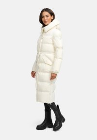 Padded long coat in soft white with a high collar, front zip closure, and side pockets, paired with black chunky ankle boots.