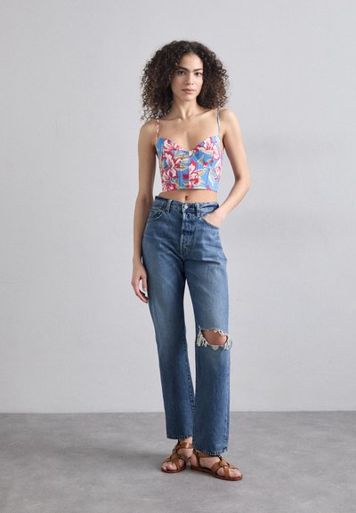 Blomster-mønstret crop top i blå, kombinert med høy midje, slitte lyseblå jeans med et hull på kneet. Brune, strappy sandaler.