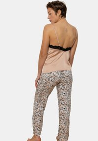 Camisole en satin dans une teinte rose avec des bordures en dentelle noire, associé à un pantalon à motif floral dans des teintes douces de beige et de noir.
