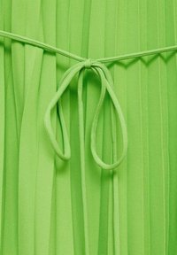 Tissu plissé vert vif avec une ceinture étroite nouée en un simple nœud au centre.