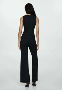 Čierny overal s tesným korzetom a širokými nohavicami. Obsahuje hladkú textúru a nenápadný zips na chrbte.