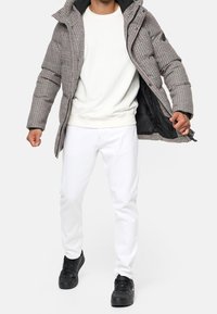 Ruudullinen toppatakki, jossa on huppu, musta vuori ja näkyvä vetoketju edessä. Päällä valkoinen collegepaita, yhdistetty valkoisiin farkkuihin ja mustiin kenkiin.