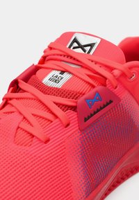 Νεον ροζ αθλητικό παπούτσι με επάνω από διχτυωτό υλικό, υφές και μπλε λεπτομέρειες. Διαθέτει επίπεδα κορδόνια και ετικέτα για την τοποθέτηση των κορδονιών.