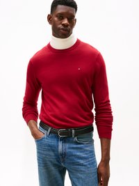 Maglione rosso a maglia con scollo rotondo, abbinato a jeans in denim blu. Presenta una sottoveste bianca a collo alto e una cintura intrecciata nera.