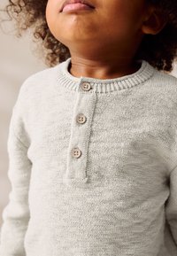 Maglione grigio chiaro lavorato a maglia con scollo rotondo, tre bottoni in legno e tessuto strutturato. Colletto a costine che aggiunge dettaglio.