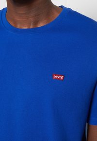 Blue cotton t-shirt with short sleeves and round neckline, featuring a red embroidered Levi's logo on the left chest area.