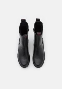 Botas de cuero negras hasta el tobillo con una superficie lisa, cierre de cremallera y tiradores en forma de bucle. Suelas de goma con un borde ligeramente elevado.
