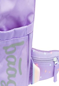 Zaino in nylon viola con una texture liscia, dotato di tasche frontali, scritte argentate e pois multicolori nell'area della cerniera.