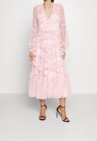 Abito midi a strati rosa con tessuto testurizzato e arricciato e maniche lunghe trasparenti. Presenta una scollatura a V e una gonna a strati. Tacchi neri con cinturini.