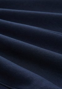 Ciemnoniebieska tkanina o gładkiej teksturze, z subtelnymi fałdami i jednolitym wzorem splotu. Brak widocznych wzorów ani elementów metalowych.