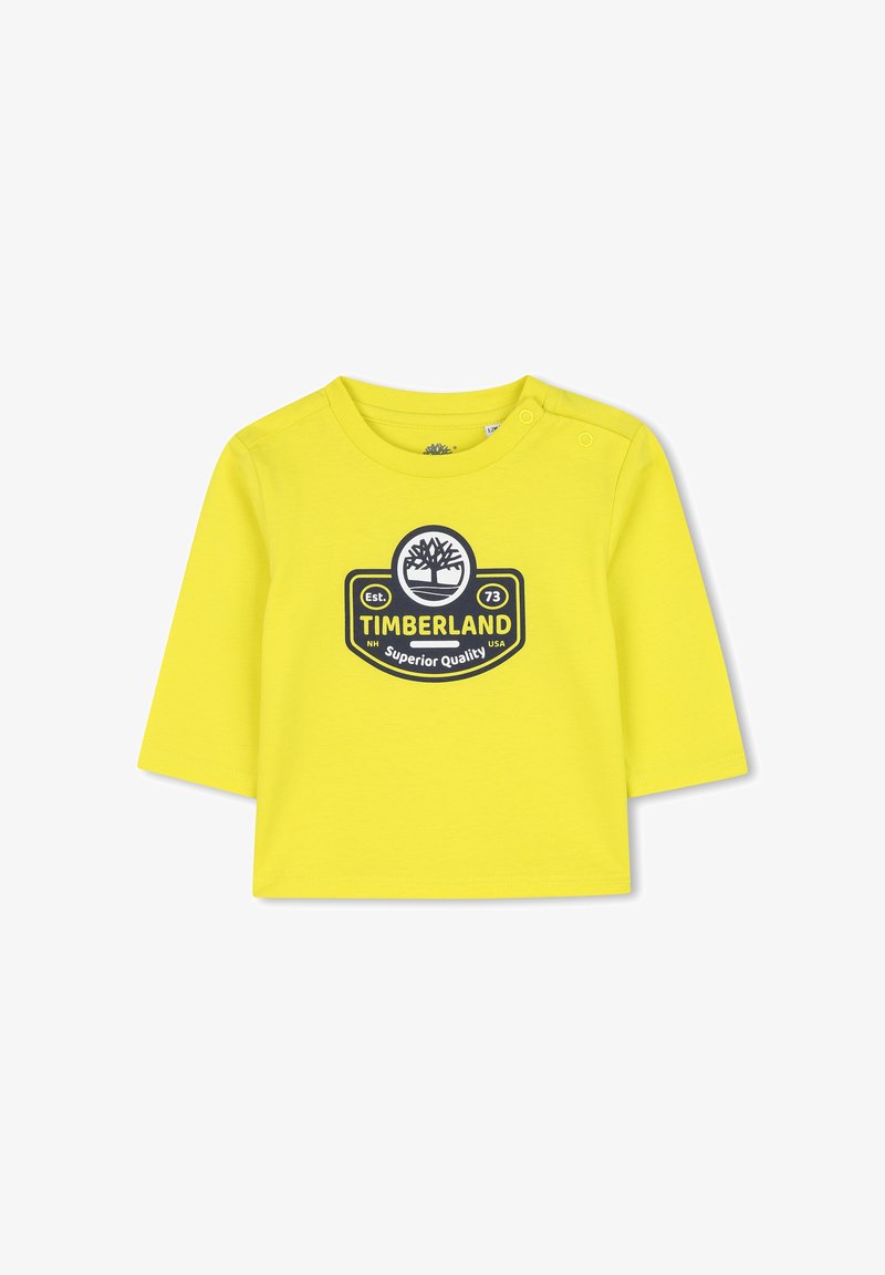 Chemise en coton jaune à manches longues avec un col rond et un logo graphique en noir. Détails de boutons-pression sur l'épaule gauche.
