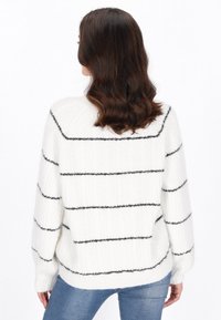 Maglione bianco lavorato a maglia con righe orizzontali nere, vestibilità rilassata, polsini a coste e texture morbida, indossato sopra jeans blu.