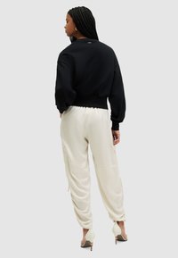 Zwarte cropped sweatshirt met lange mouwen, gecombineerd met losse crèmekleurige broeken, beide gemaakt van zachte materialen. Hakken maken de outfit compleet.
