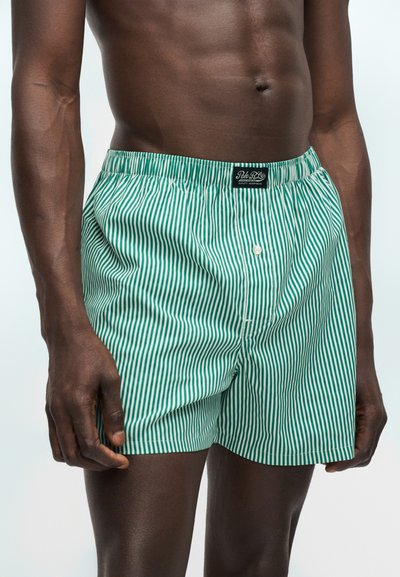 Ανδρικός κορμός που φοράει πράσινα και λευκά κατακόρυφα ριγε μποξεράκια με μια μαύρη ετικέτα στη λαστιχένια μέση.