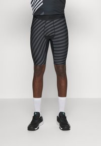 Pantalones cortos deportivos de rayas negras y grises con un corte de longitud media, que presentan un ajuste ceñido y una cintura elástica, combinados con zapatillas negras y calcetines blancos.