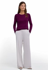 Top viola a maniche lunghe abbinato a pantaloni larghi color grigio chiaro. Il top ha una scollatura rotonda; i pantaloni hanno tasche laterali e una texture fluida.