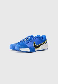 Blå idrettssko med en teksturert mesh-overdel, gule detaljer og en svart Nike swoosh. Har en mønstret gummisåle for godt grep.