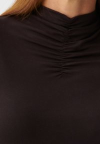 Schwarzes Oberteil mit hohem Halsausschnitt, das in der Mitte mit gerafftem Stoffdetail versehen ist, aus glattem, elastischem Material gefertigt.