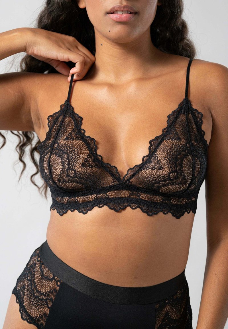 Mustat pitsinen bralette, jossa on aaltoilevat reunat, ohuet hihat ja herkkä kukkakuosi. Yhdistetty korkeavyötäröisten mustien alaosien kanssa.