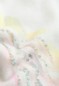 Witte stof met een subtiel pastelpatroon heeft iriserende pailletten in golvende lijnen, waardoor textuur en visuele interesse ontstaan.