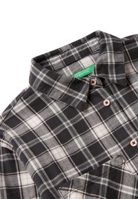 Camicia a quadri bianca e nera con bottoni marroni e etichetta verde ben visibile dei United Colors of Benetton sul colletto interno.
