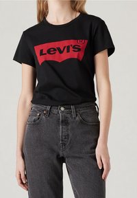Camiseta negra con un logo rojo de Levi's. Combinada con unos vaqueros de tiro alto y deslavados en negro. Diseño simple con escote redondo.