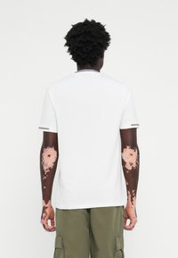T-shirt blanc à manches courtes avec un col rond, présentant un accent gris au niveau du col. Tissu en coton lisse, porté avec un pantalon cargo olive.