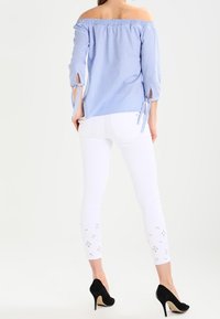 Jasnoniebieska bluzka w paski z odkrytymi ramionami, elastycznym dekoltem, rękawami do łokcia i wiązaniami. Dobraną do niej białe dopasowane spodnie z kwiatowymi wycięciami.