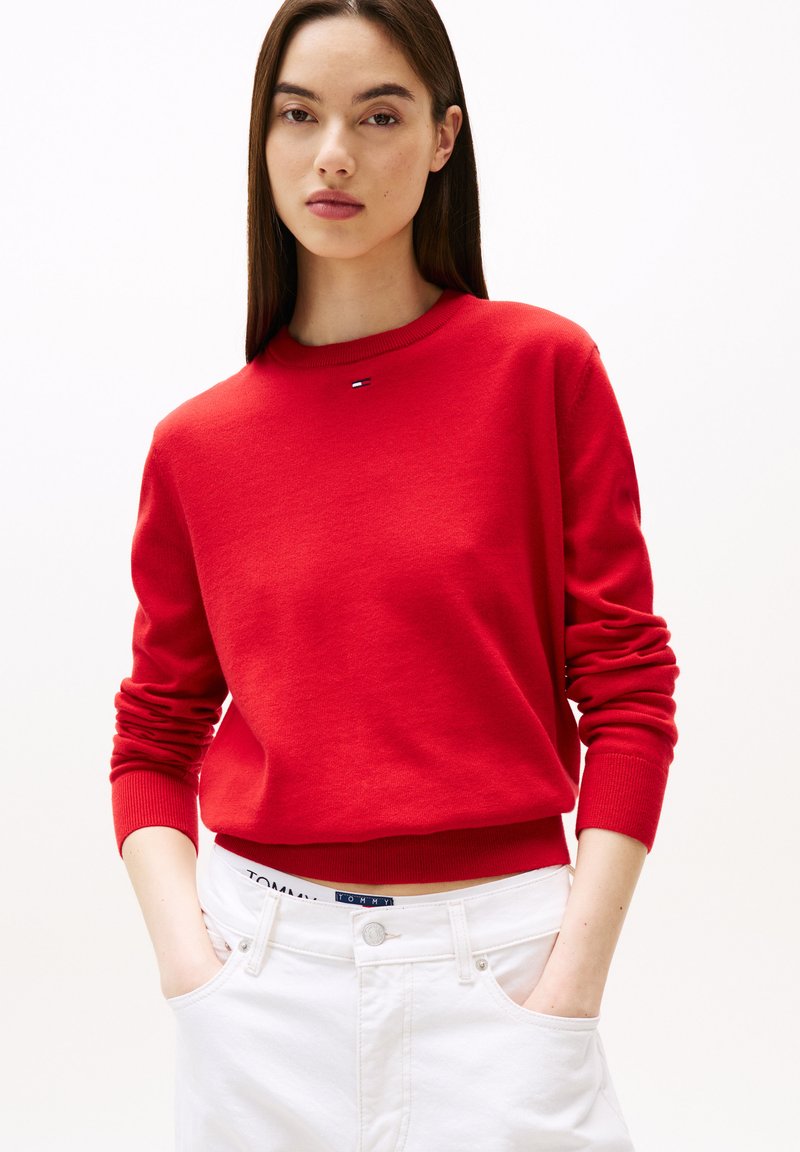 Felpa rossa realizzata in tessuto morbido, con scollatura rotonda e polsini a costine. Presenta un piccolo logo sul petto. Abbinata a jeans bianchi.