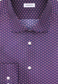 Camicia a maniche lunghe di colore viola con bottoni, con un motivo circolare ripetuto in bianco e rosa, dotata di etichetta "seidensticker" all'interno del colletto.