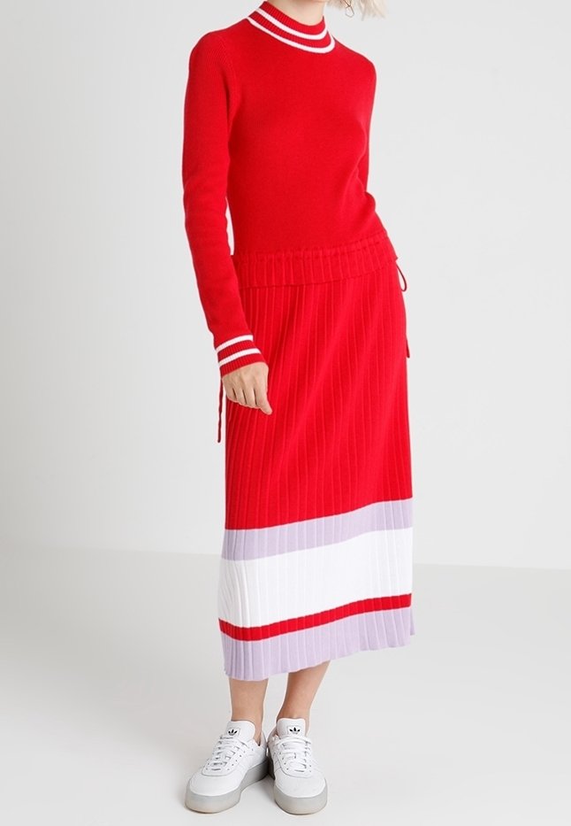 Rotes Strickoberteil mit einem weißen und roten gestreiften Kragen, kombiniert mit einem roten Faltenrock, der horizontale Farbblöcke in Weiß und helllila aufweist.
